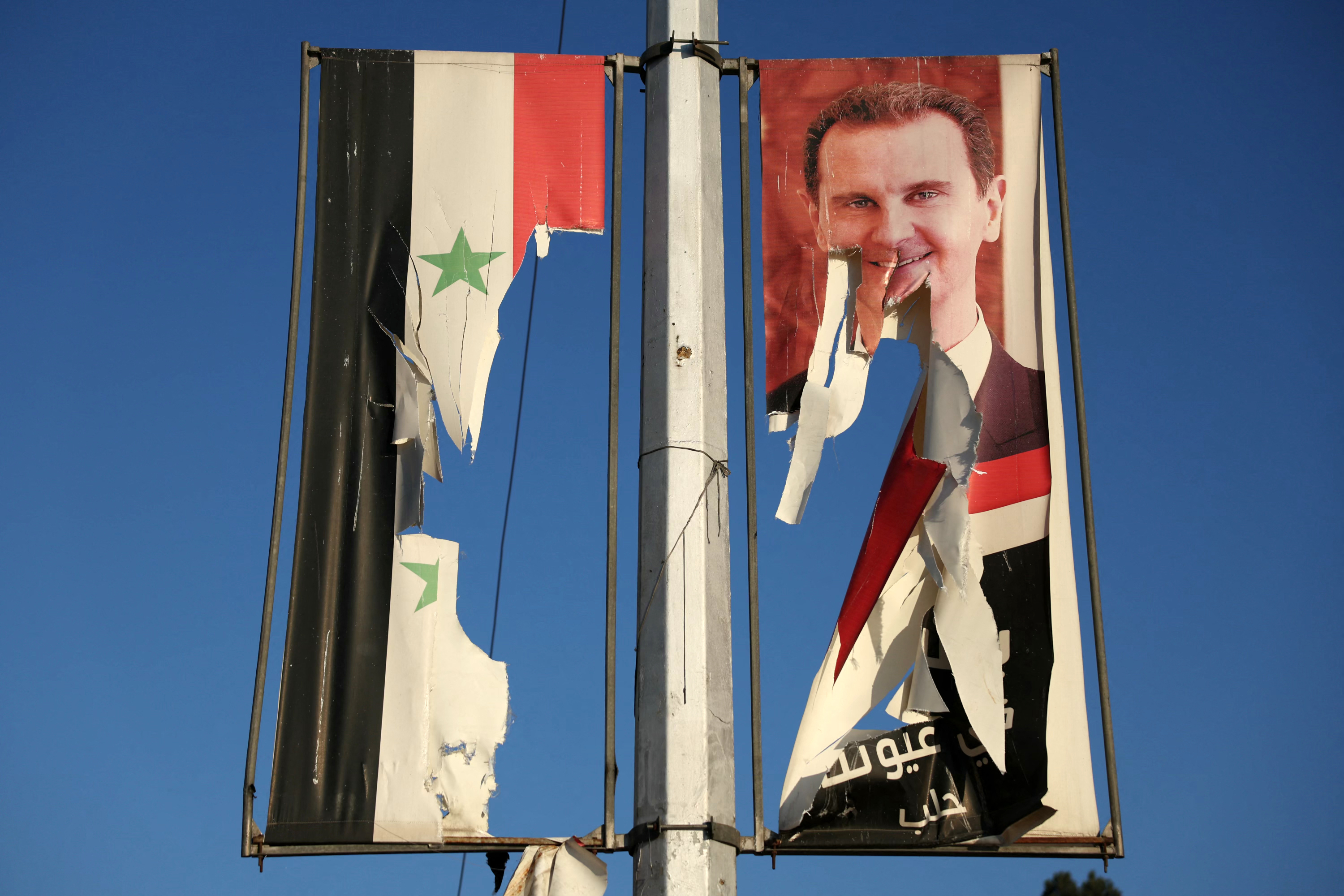 Una valla publicitaria con la imagen del presidente sirio Bashar al-Assad y una bandera nacional son arrancadas por combatientes antigubernamentales en Alepo.