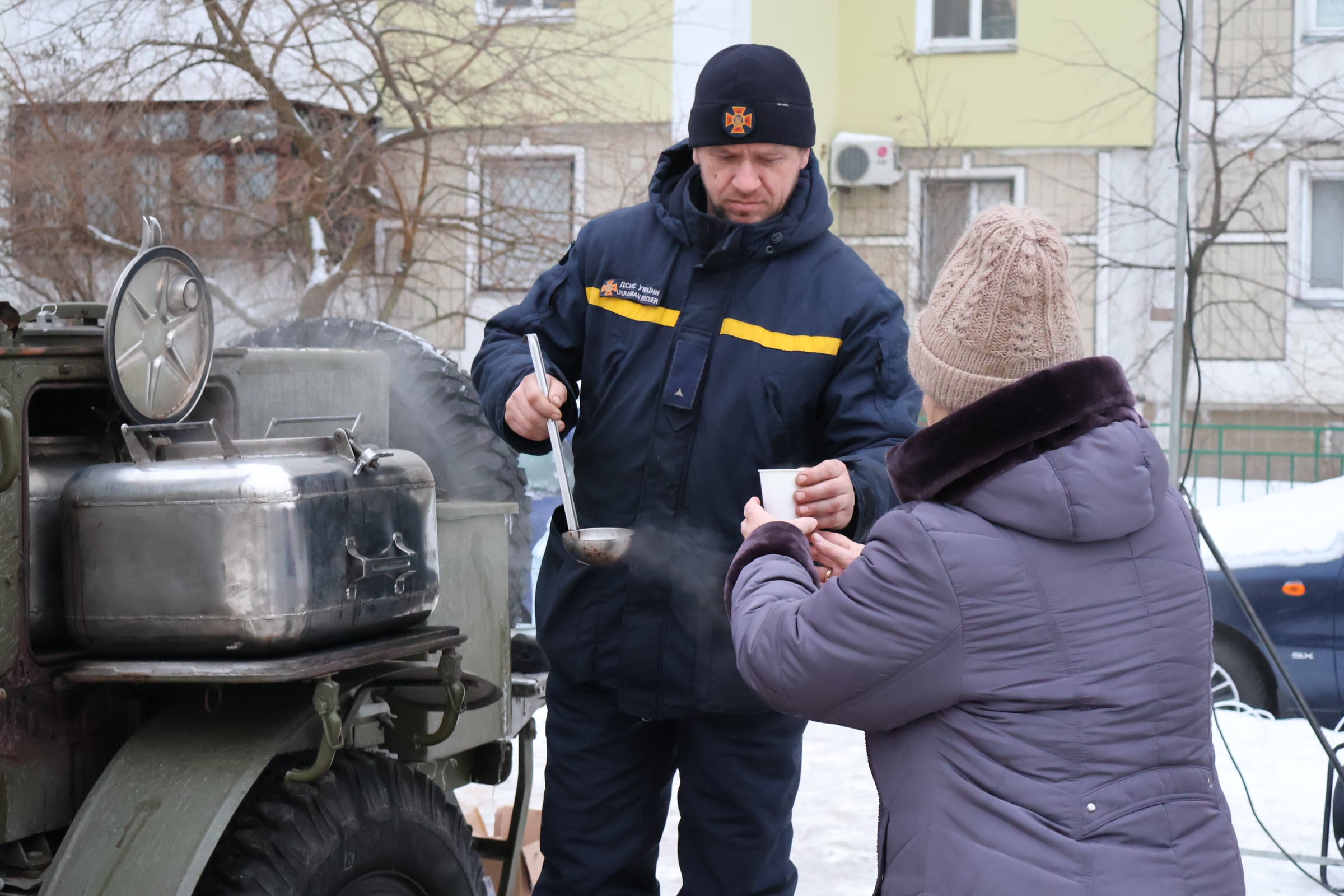 Un empleado del Servicio de Emergencias de Ucrania sirve una taza de agua caliente a una mujer en el barrio de Troiéshchina, en Kiev.