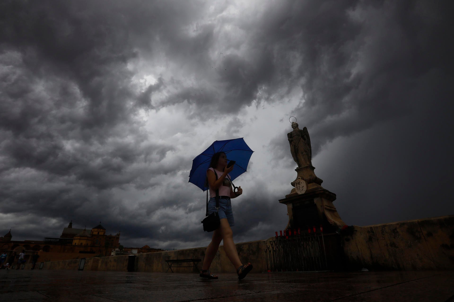 Una mujer se protege de las lluvias caídas esta tarde mientras pasea por el puente romano de Córdoba. (EFE/Salas)