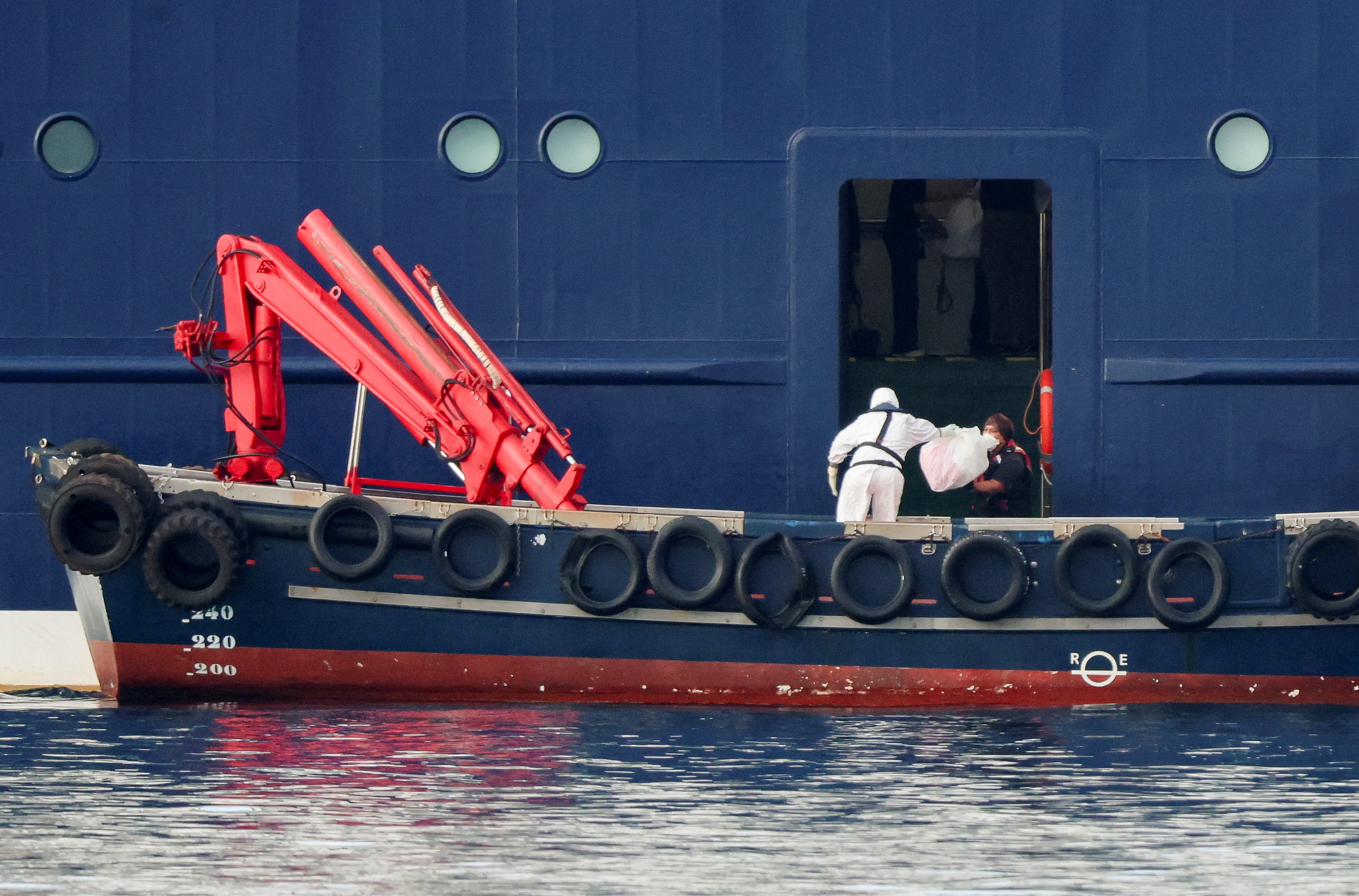 Una persona con equipo de protección individual (EPI) transfiere un paquete al crucero MV Hondius desde una embarcación en el puerto de Granadilla de Abona, tras el brote de hantavirus que afecta al buque, en Tenerife, España, el 10 de mayo de 2026. (Reuters/Hannah McKay)
