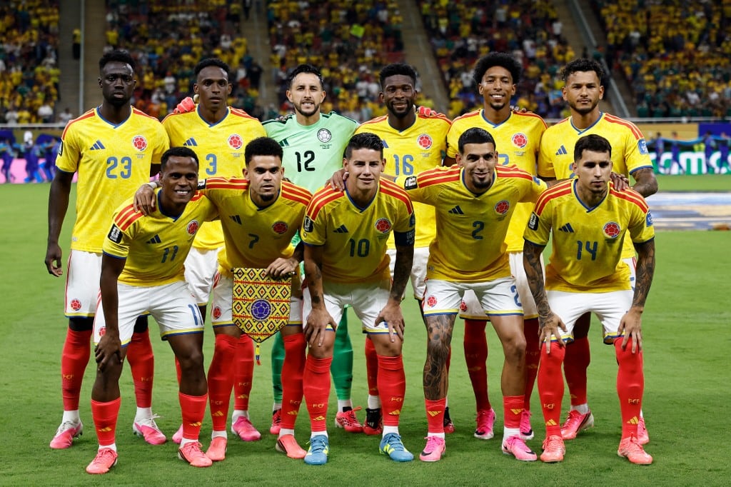 Once jugadores de la selección nacional de fútbol de Colombia posan uniformados con su camiseta amarilla en el césped de un estadio antes de un encuentro, con las tribunas de fondo. (Ulises Ruiz)