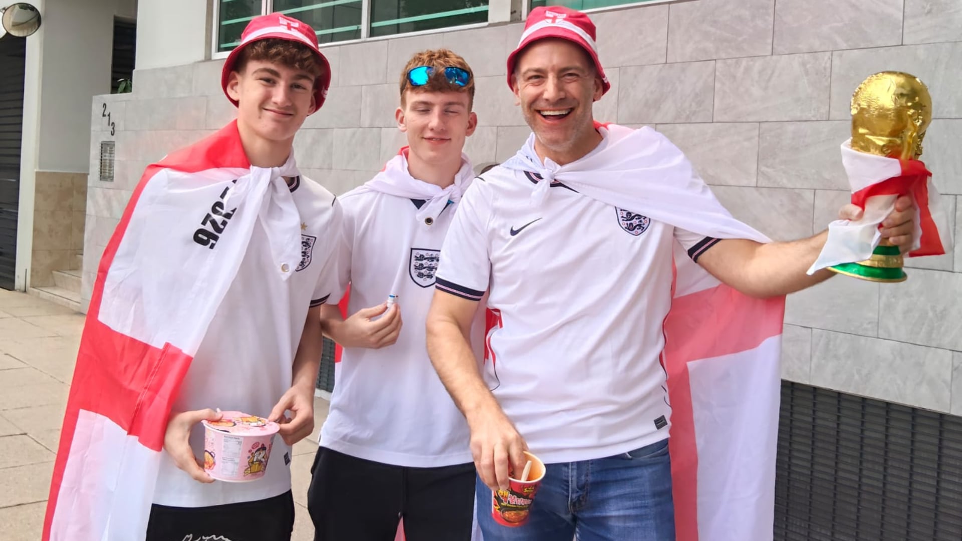 Tres aficionados de Inglaterra, con camisetas, banderas y gorros con los colores de su selección, portan una réplica del trofeo mundial en su camino hacia el Ángel de la Independencia en México. (Néstor Hernández )