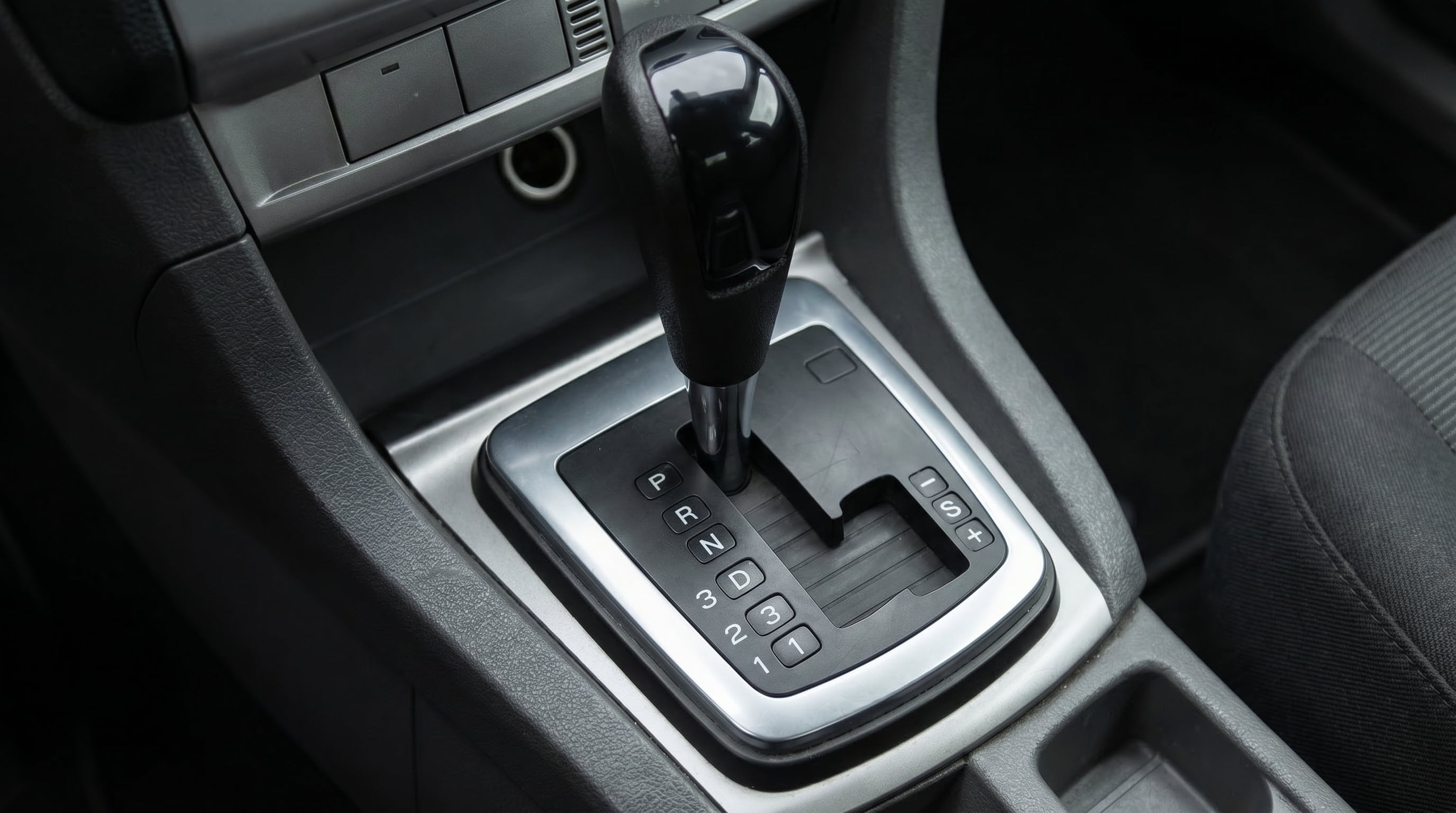 Una palanca de cambios de coche automático con las posiciones P, R, N, D, y las opciones de marcha manual 3, 2, 1 y +/- se muestra en detalle, destacando su diseño funcional en el interior del vehículo. (Imagen Ilustrativa Infobae)